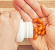 hands pouring orange coenzyme Q10 pills from bottle into palm