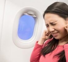 Woman holding her ears in pain while experiencing airplane ears while flying