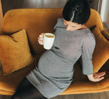 Pregnant woman sitting on sofa drinking coffee