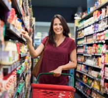 Woman holds red basket, shopping in grocery store aisle