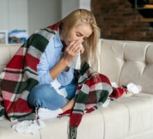 woman sitting on couch surrounded by tissues because of influenza