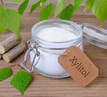 Glass container with white crystals of xylitol, birch branches nearby; non-sugar sweeteners