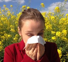 woman with spring allergies blowing nose in a field of wildflowers