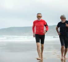 Two older men jogging barefoot along the beach.