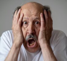 A disoriented man with memory problems and dementia holding his face is dismay
