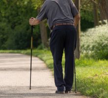 frail man walking with difficulty with walking sticks