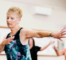 Older woman in an exercise class extending her arms sideways during a group fitness dance class.
