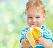 smiling toddler peeling and eating banana early foods