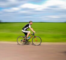 Man riding a bicycle on a rural road with green fields in the background.