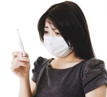 Sick Chinese woman with thermometer and wearing a face mask