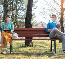 Man and woman wearing face masks sitting at either end of a park bench