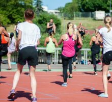 Group of people doing a Zumba fitness class outdoors on a basketball court.