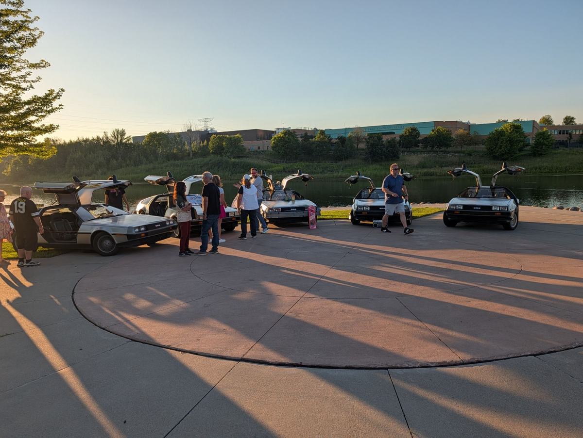 Group photo of the DeLorean team standing with their cars