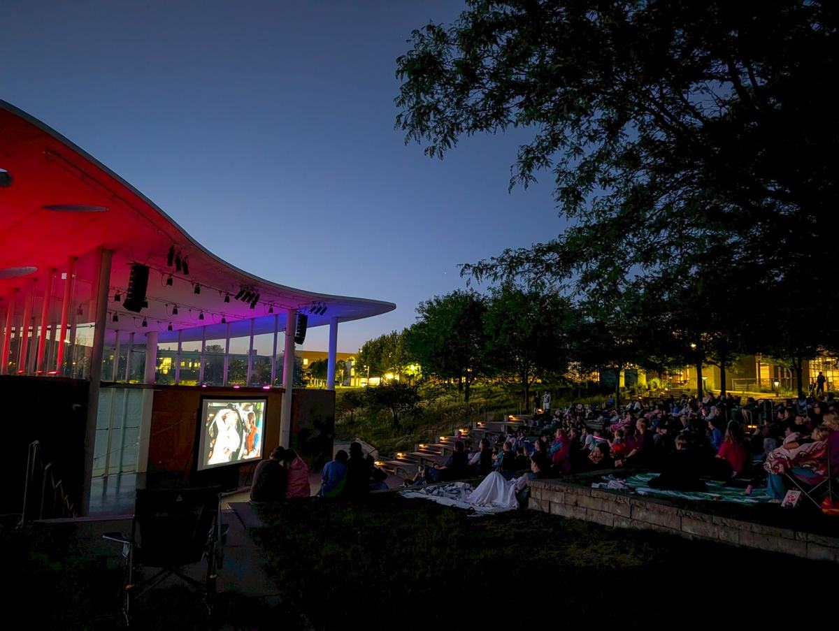 Audience sitting and standing in the park watching Back to the Future on a big screen