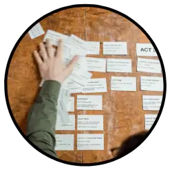 A screenwriter using a classic outlining tool: 3x5 index cards on a bulletin board to outline their screenplay. The writer adds a new outline beat to board that has groups of cards separated by Act.