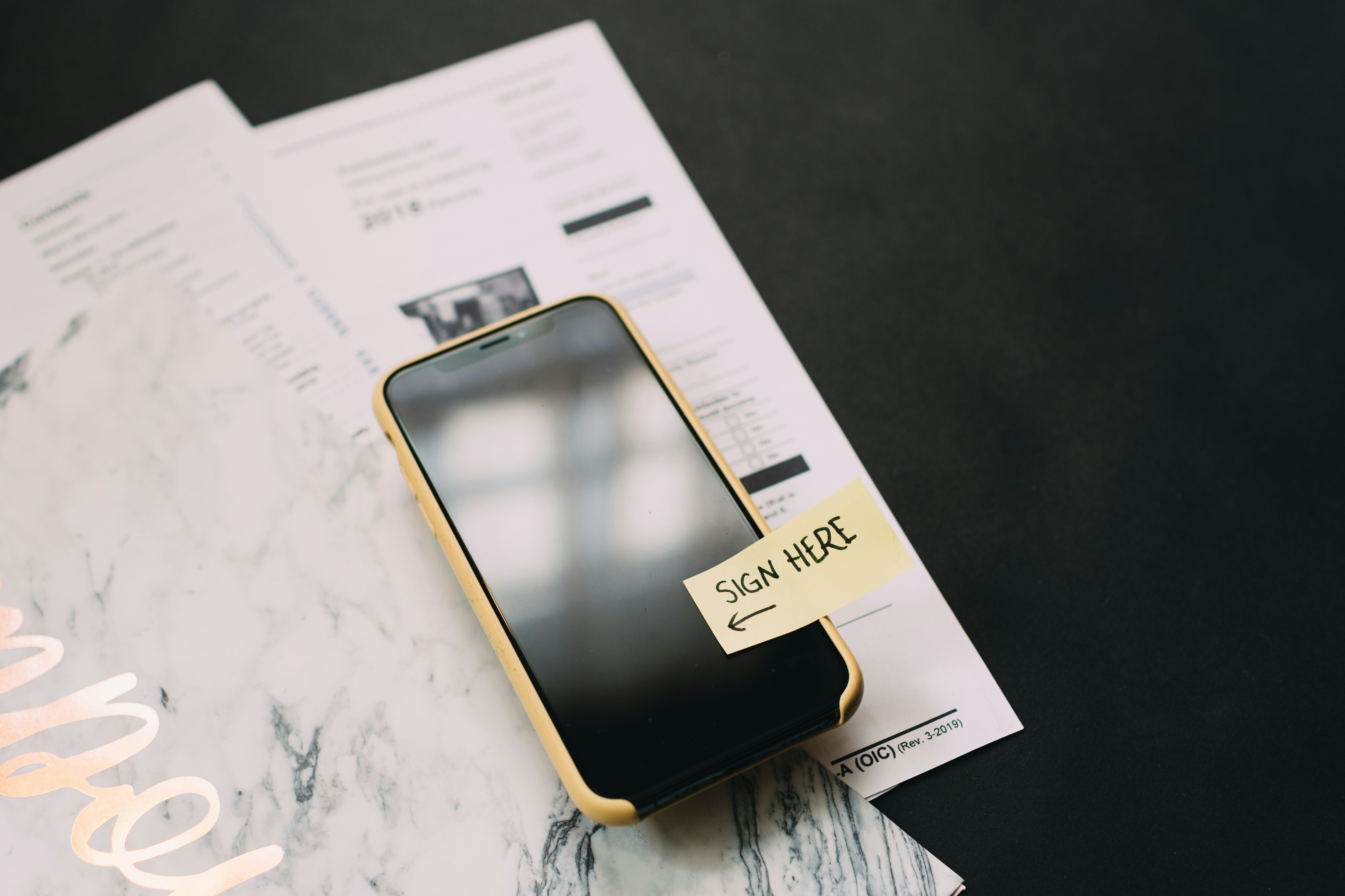 Paper form and folder with a phone sitting on top and a sign here sticker on the screen. Image by Kelly Sikkema