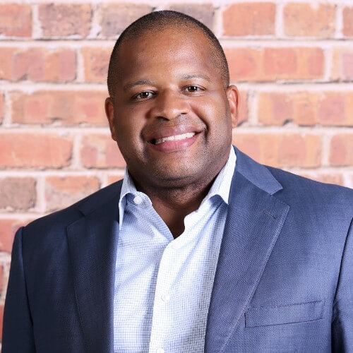 A smiling man with short hair, wearing a button up shirt and a jacket, in a professional headshot.