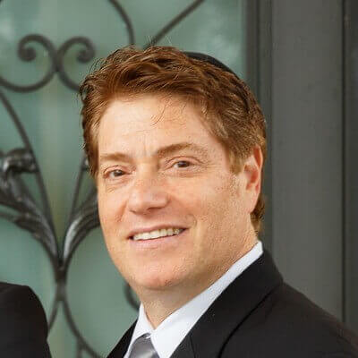 A cheerful man wearing a dark suit, in a professional headshot.