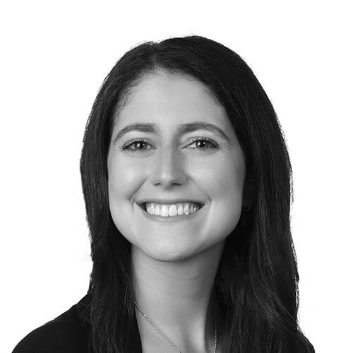 A black and white headshot of a woman with straight, long dark hair and a bright smile.