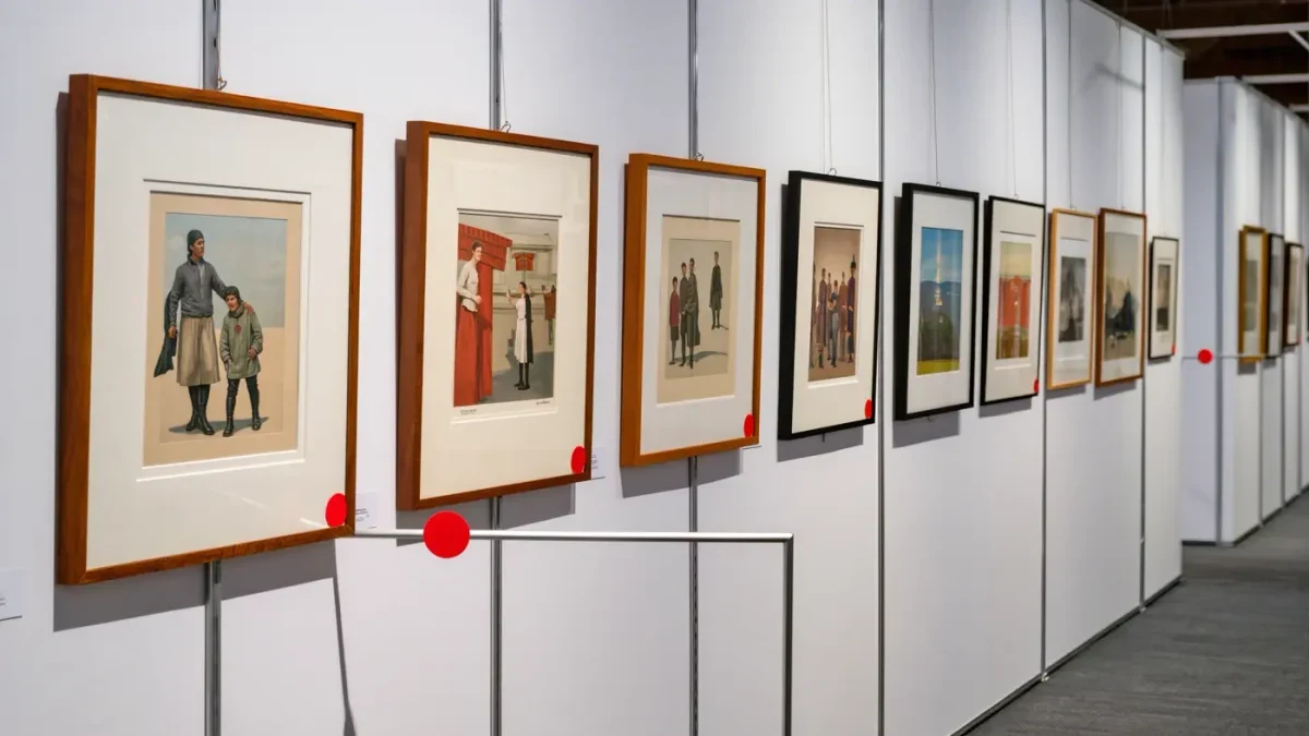 Red sold dots beside small framed works on a fair booth wall