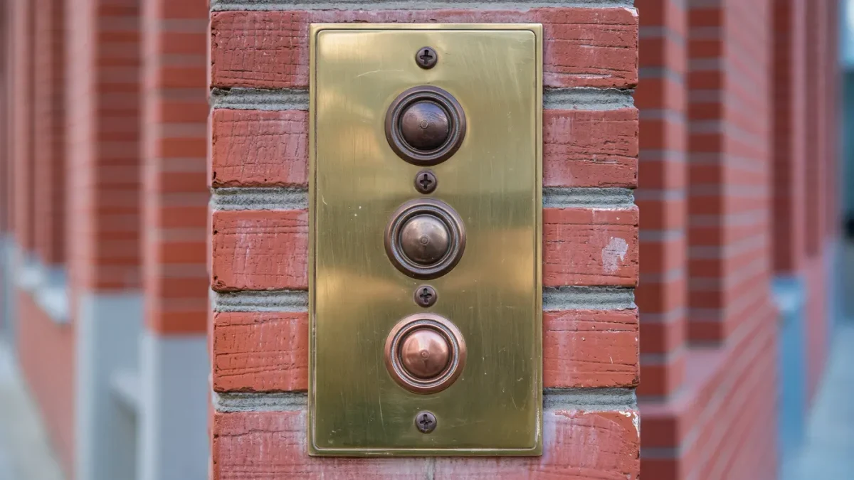 Close-up of a brass doorbell panel on a small brick apartment building
