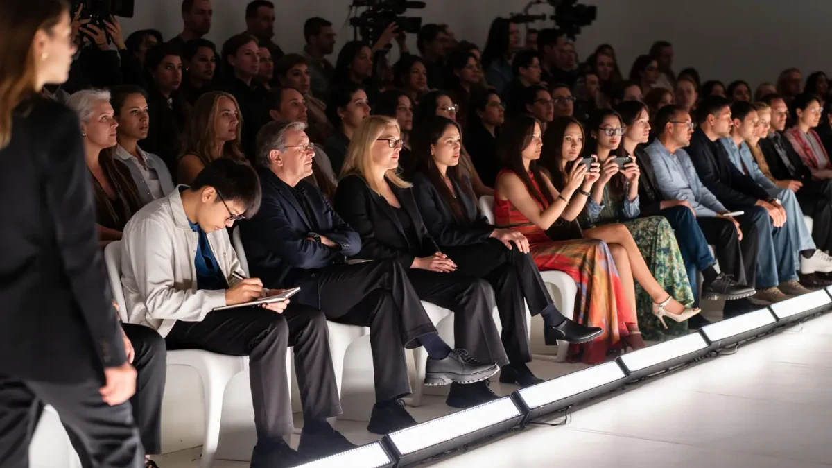 Front-row audience leaning forward with phones and notebooks as a model passes