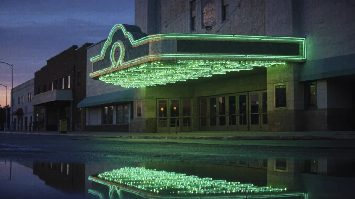 Green-lit theater entrance at dusk on an empty street