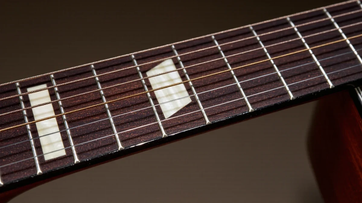 Close-up of pearl inlay dots on a dark guitar fretboard under showroom light