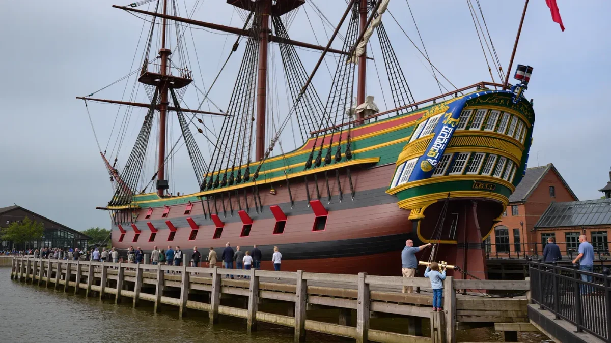 Visitors walking beside a wooden sailing ship at a maritime museum dock