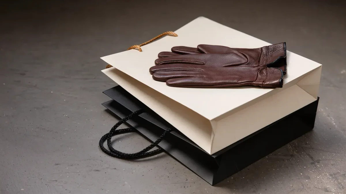 Blank luxury paper shopping bags stacked with leather gloves on stone