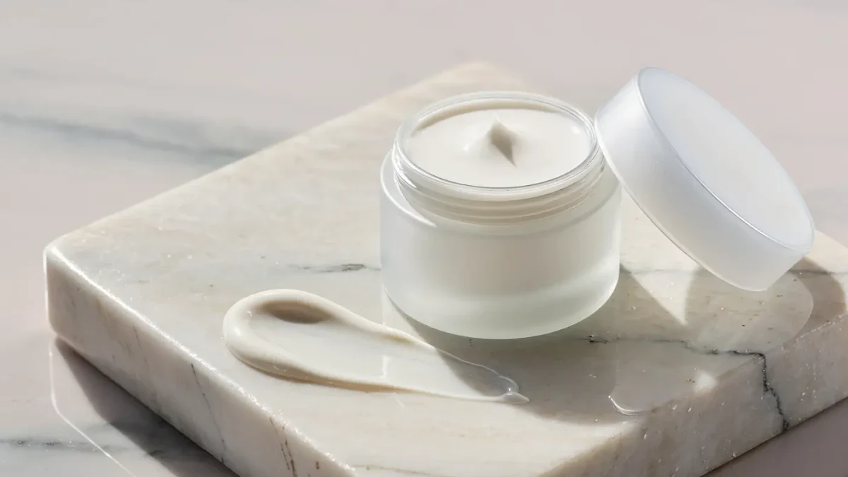 Small white eye cream jar with open lid on a marble surface in studio light