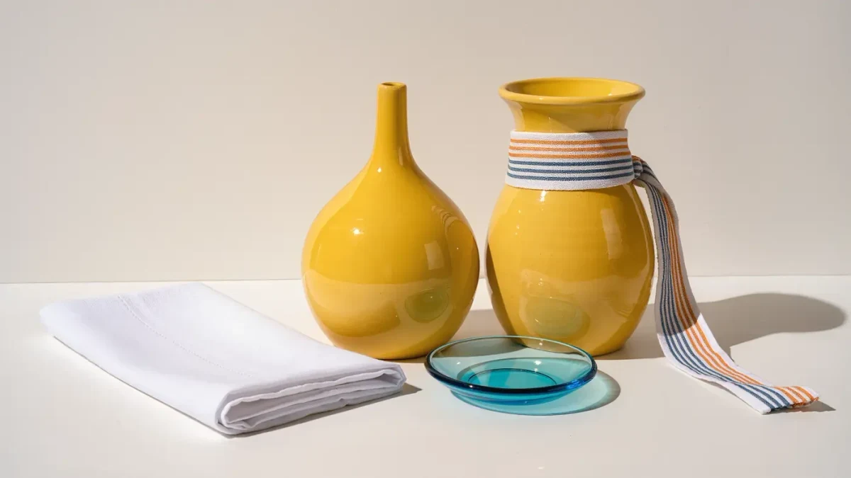 Studio still life of two sunny yellow vases, one striped and one plain, with bright white and sky blue accents on a light surface
