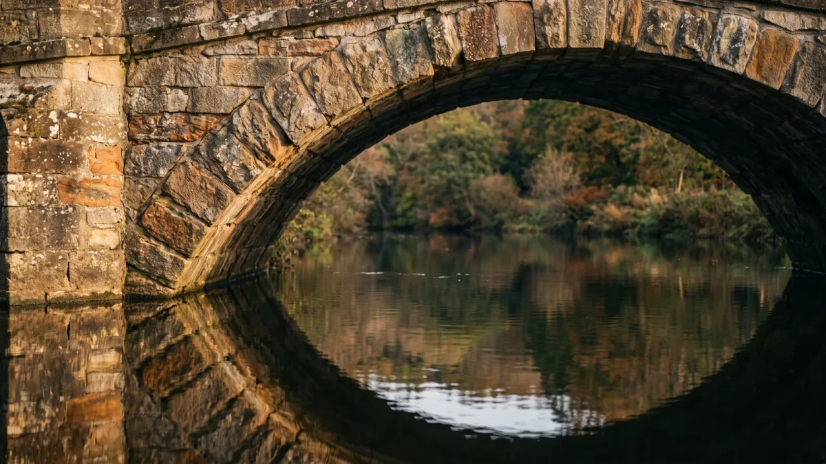 Close-up of a weathered stone bridge arch over still water
