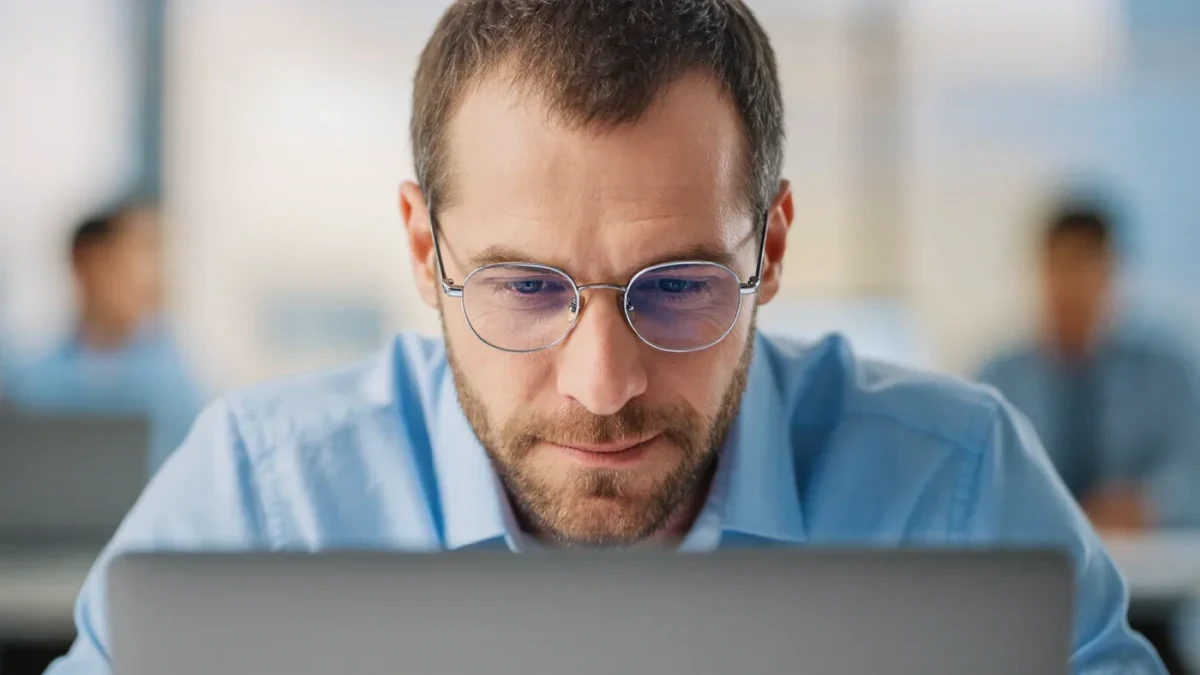 Businessman squinting skeptically at a laptop in an office
