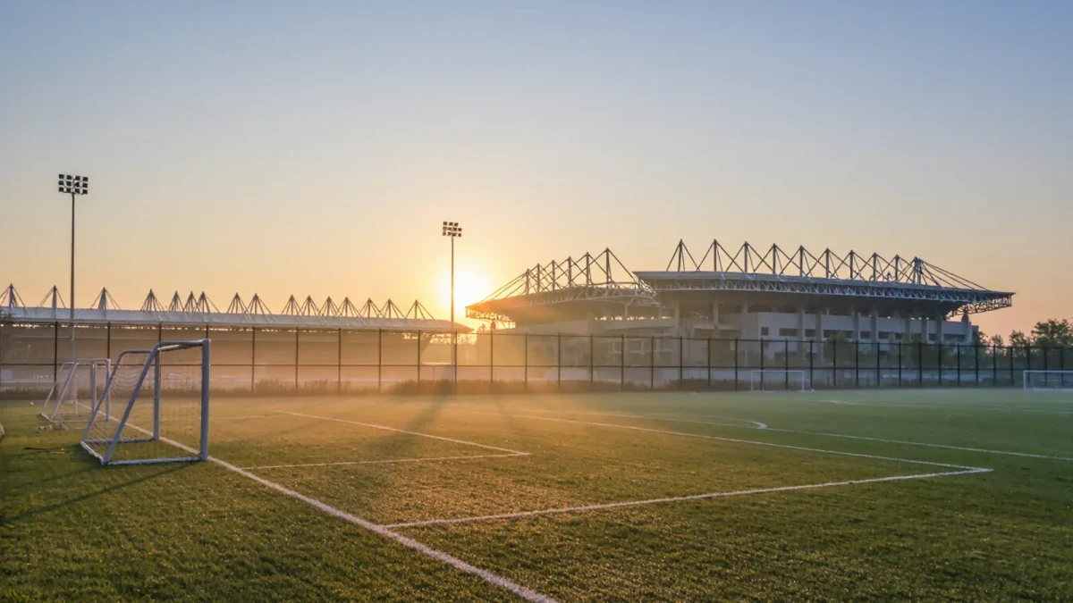Academy pitch beside a main stadium at dawn, unoccupied