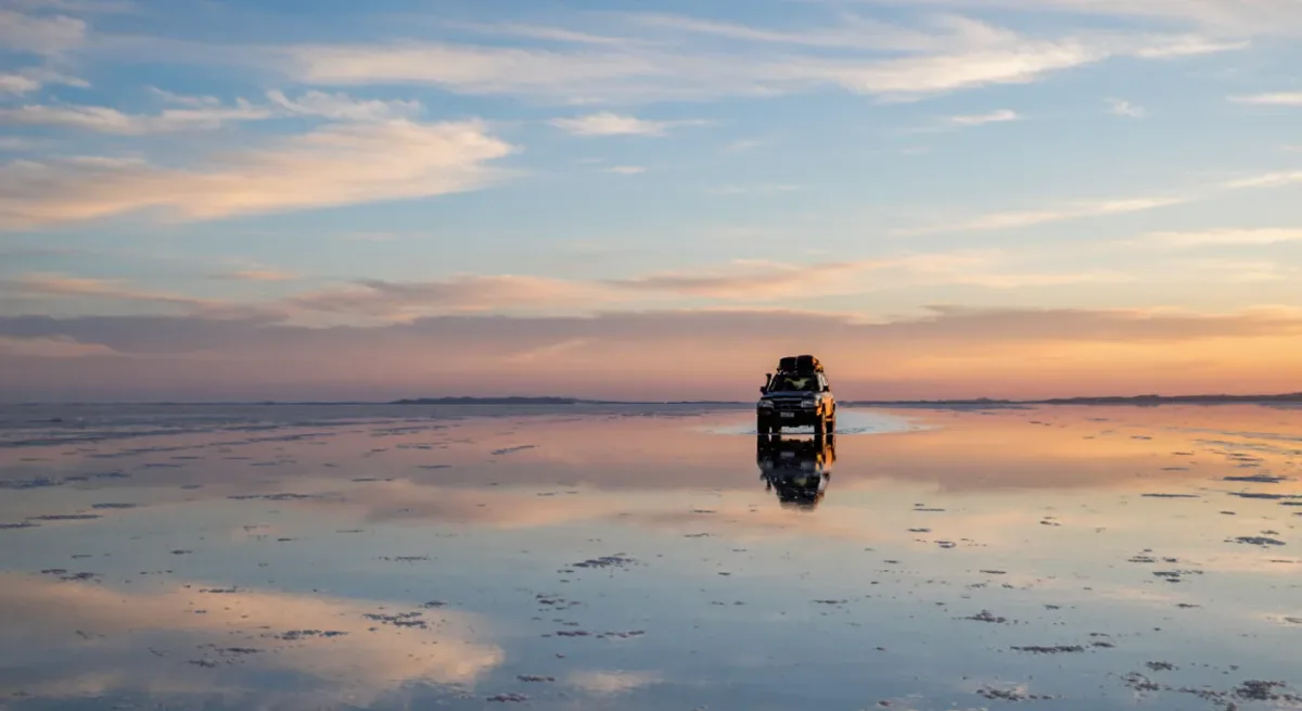 Jeep tracks crossing the flooded salt flat mirror at dusk
