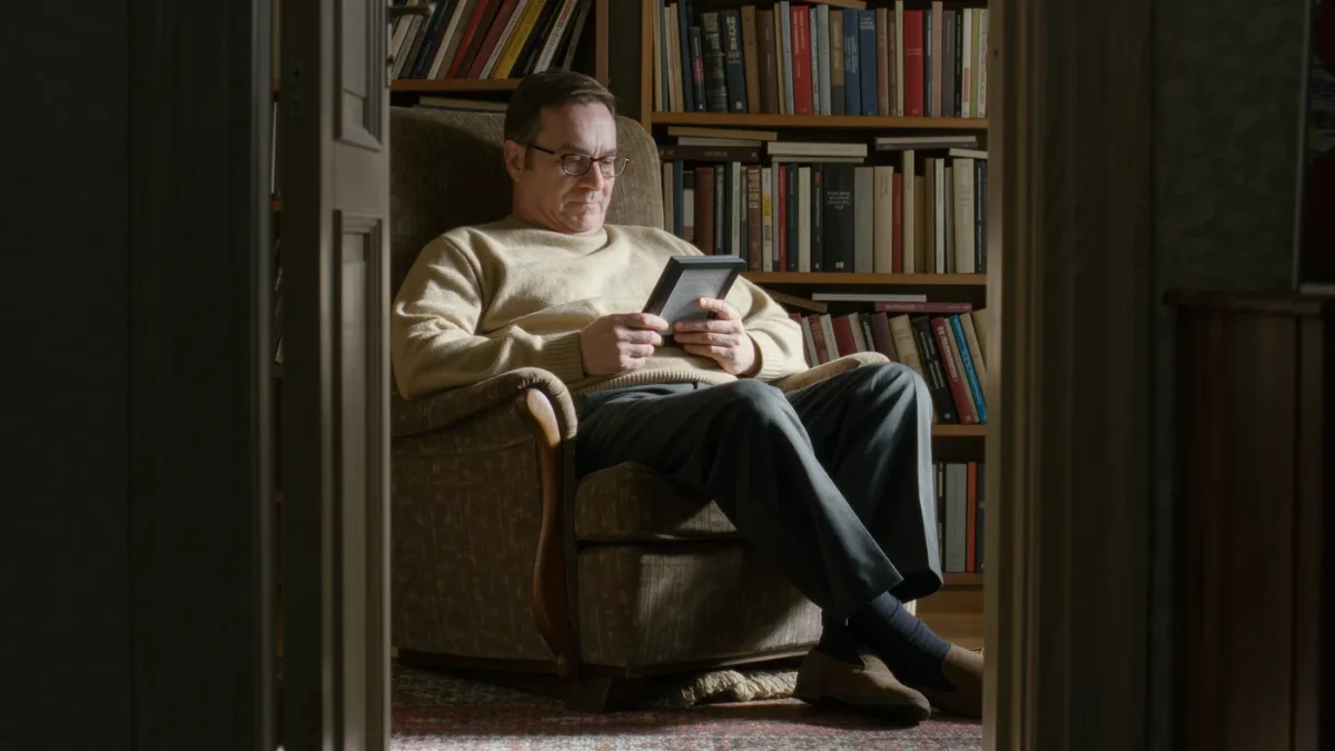 Older man reading on a generic e-reader in an armchair by a window