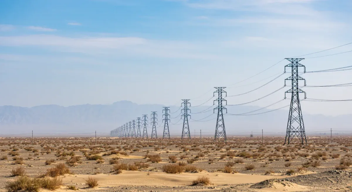 Transmission towers crossing desert terrain toward the horizon
