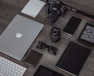 Tablet, phone, camera with lens and a notebook with a pen.