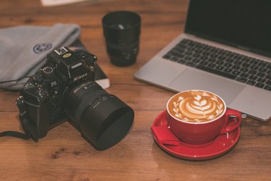 A cup of coffee, camera and a laptop.