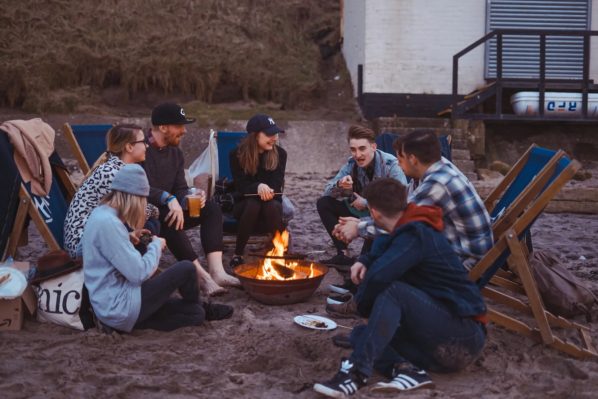 A group of friends huddled around a fire on the beach having fun.