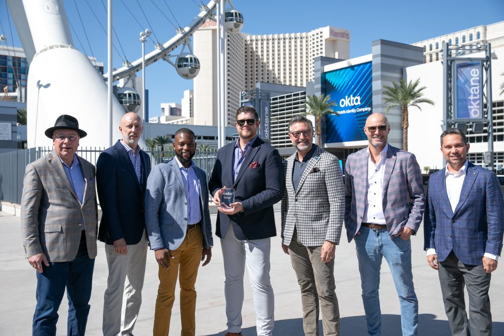 Seven men in blazers holding an Okta award trophy outside the Oktane conference in Las Vegas