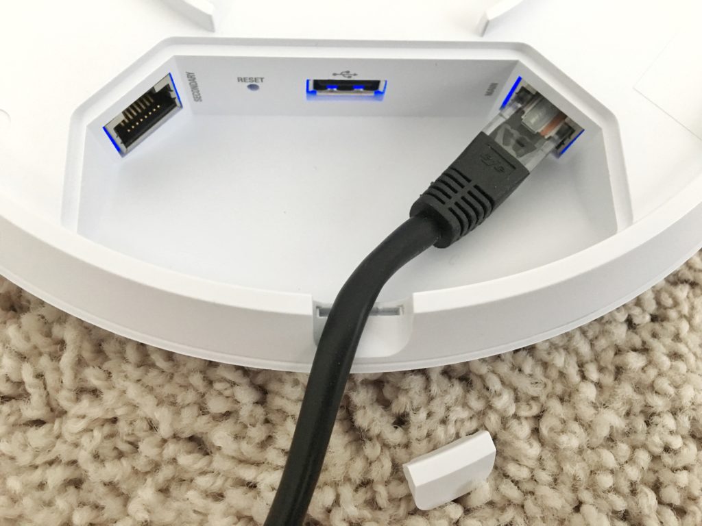 UniFi access point port bay with secondary Ethernet port, reset button, USB port, and a cable in the main port