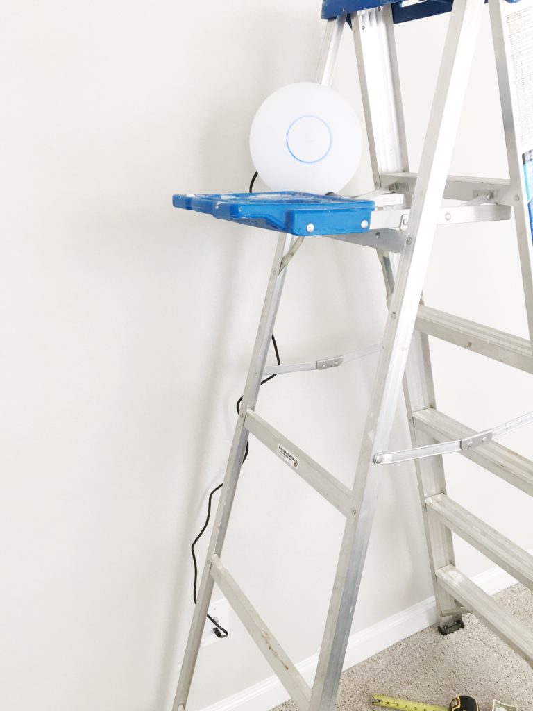 UniFi access point resting on top of a stepladder, cabled to an outlet-height wall jack to test signal at height