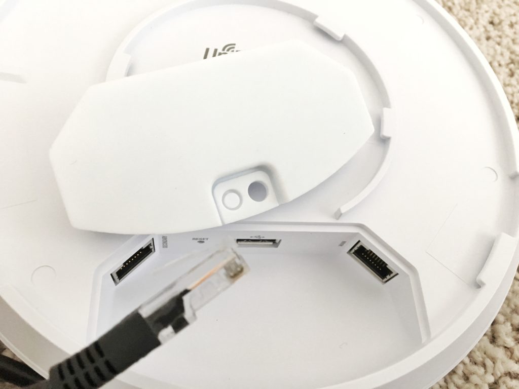 UniFi access point with its rubber port cover lifted and an RJ45 cable end beside the secondary, USB, and main ports