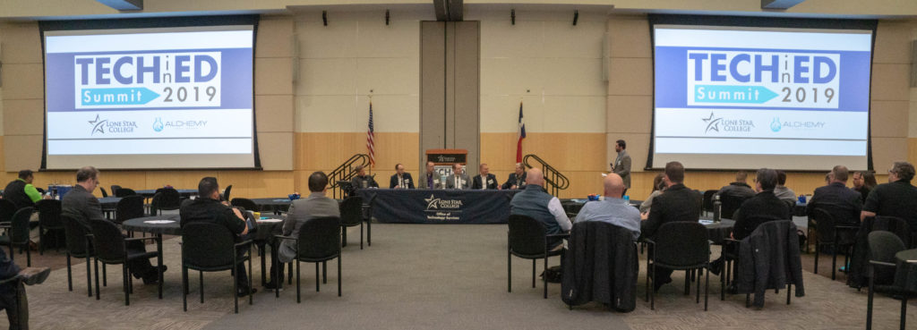 Tech-in-Ed Summit 2019 room at Lone Star College, with attendees at round tables facing the panel stage and two screens