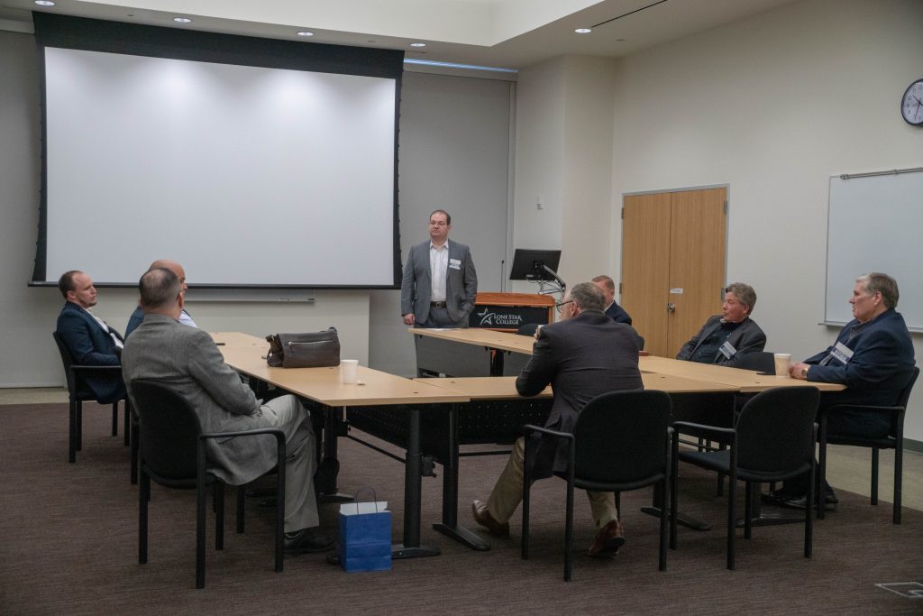 Executive panelists and attendees seated around conference tables as the breakout moderator stands at the front
