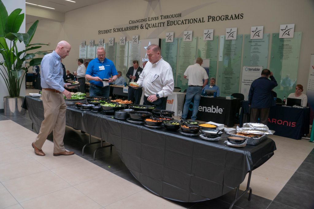 Attendees at the lunch buffet in the Lone Star College lobby, with Tenable, Varonis and other sponsor tables behind